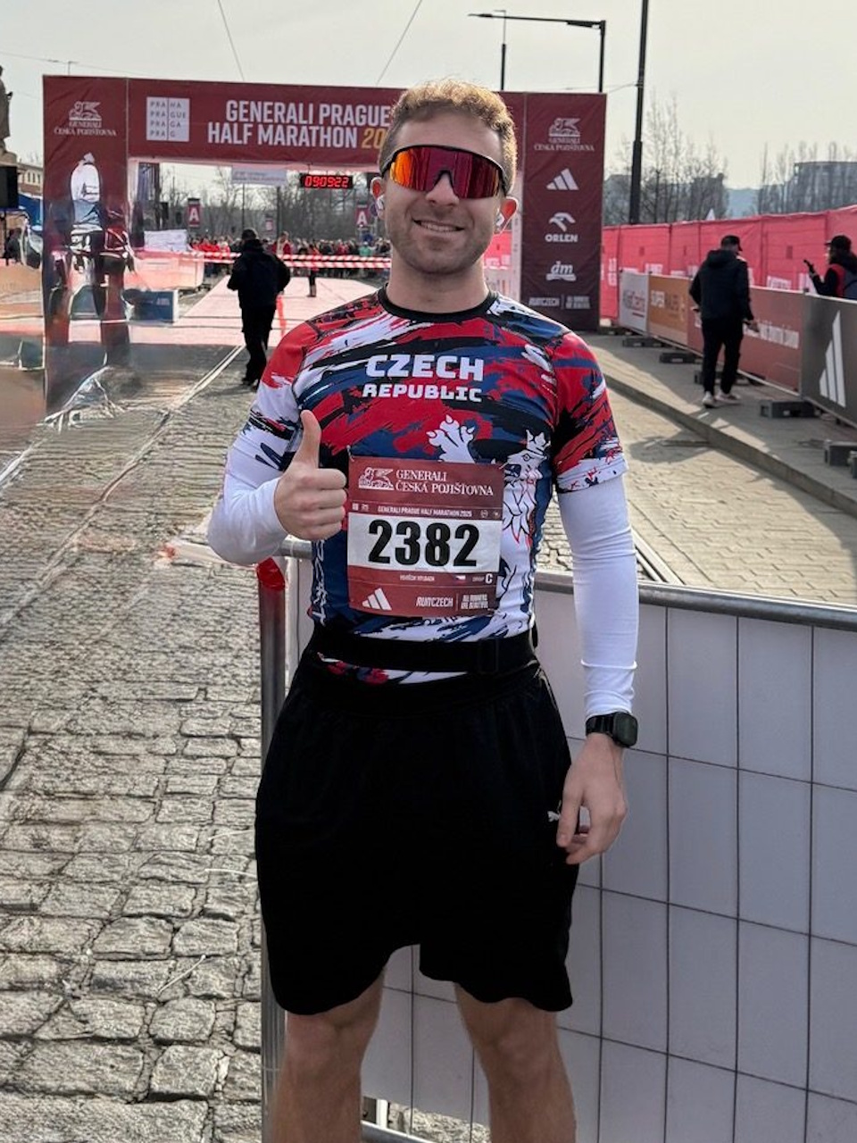 Trkač sa startnim brojem i sportskim naočalama ispred cilja utrke